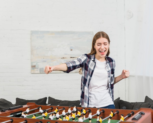 Happy young woman cheering while playing table soccer at home