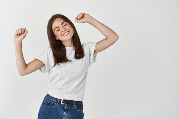 Happy young woman dancing and having fun, smiling and expressing positive emotions, standing over white wall