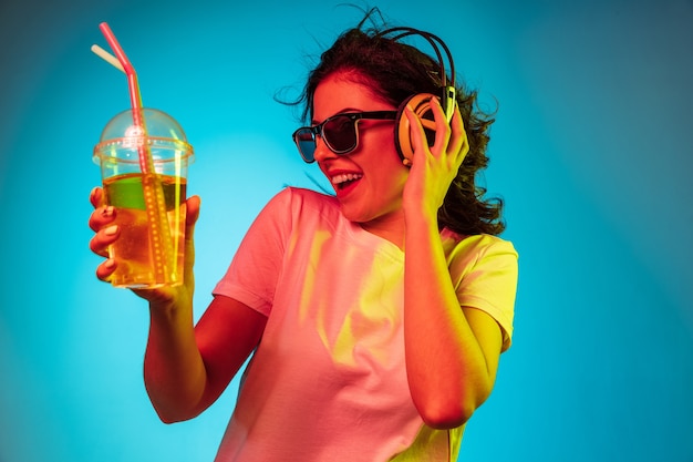 Free photo happy young woman dancing and smiling in headphones over trendy blue neon