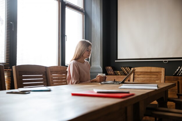 Happy young woman drinking coffee while work with laptop