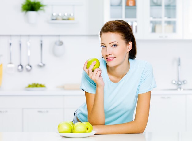 Счастливая молодая женщина ест яблоки на кухне