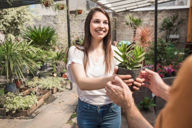 Счастливая молодая женщина дает растение в горшке своему клиенту в теплице