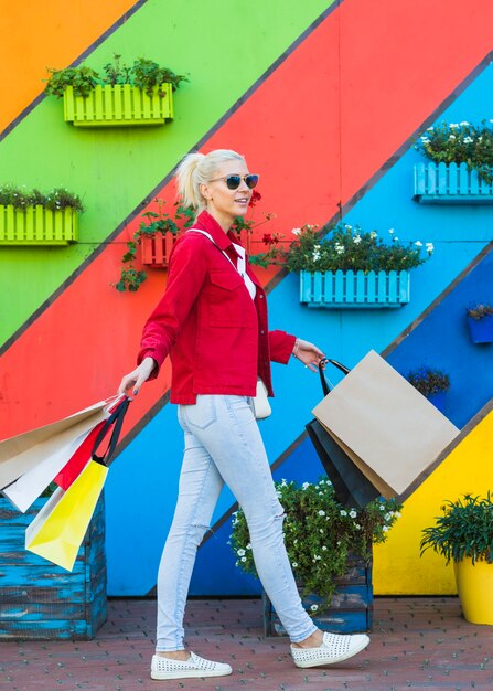 Free photo happy young woman going with bags near wall