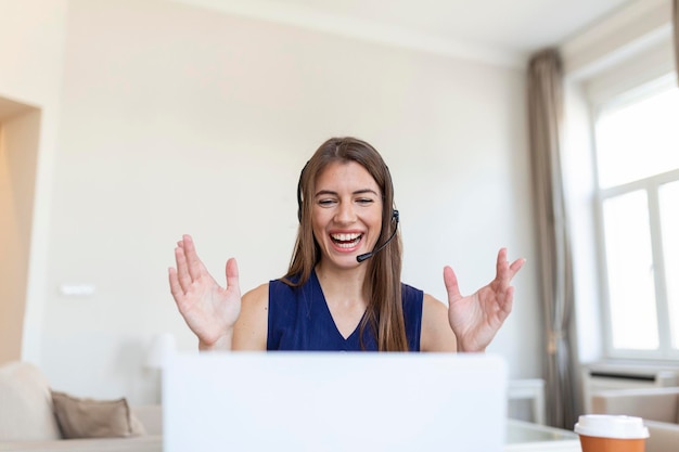 ヘッドフォンで話す幸せな若い女性がノートパソコンを見てメモをとるビジネス電話会議で話すウェブカメラによる会議オンライントレーニングecoachingコンセプト