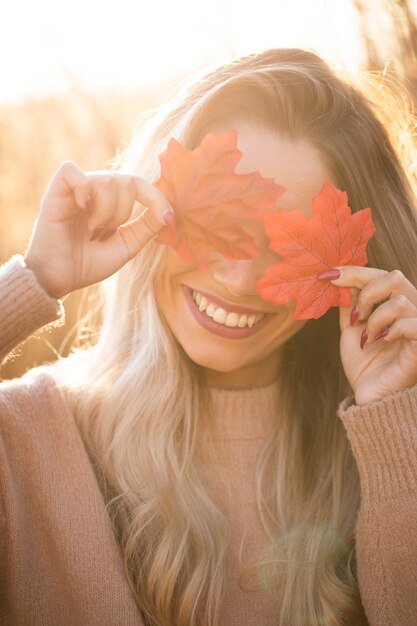 屋外でカエデの葉と彼女の目を隠して幸せな若い女