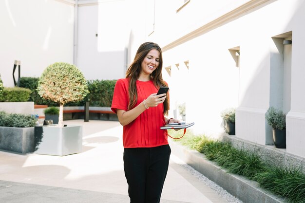 Happy young woman holding cellphone near residential building