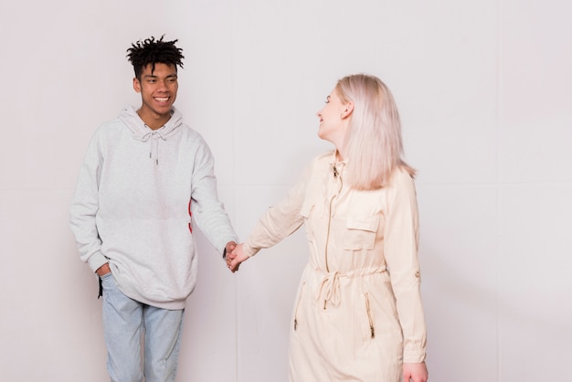 Happy young woman holding hand of her boyfriend looking at her boyfriend against white background