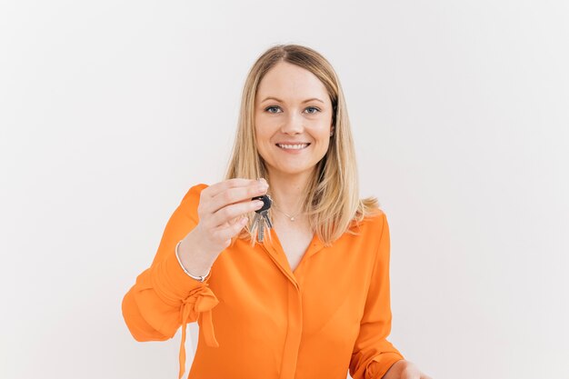 Happy young woman holding keys against white wall