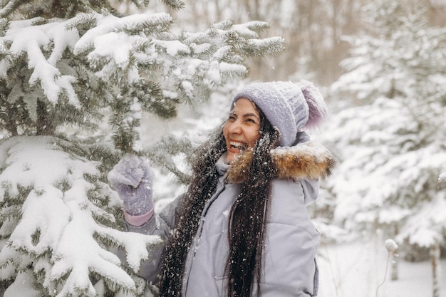 Счастливая молодая женщина зимой на прогулке на природе. женщина в сиреневой куртке стоит возле елок в зимнем парке. Premium Фотографии