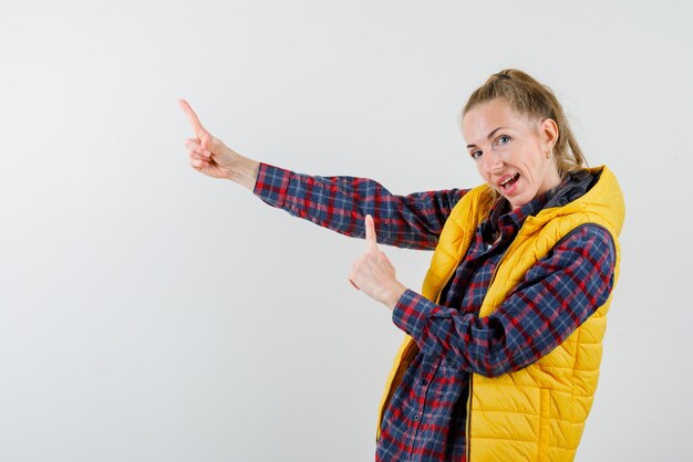 The happy young woman is pointing to left with forefinger on white background