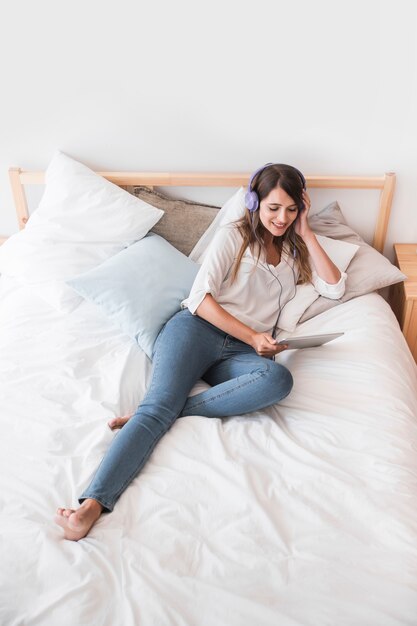 Happy young woman listening music on the bed