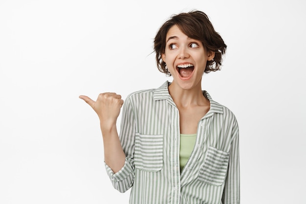 Happy young woman look and point left with amazed face standing on white.