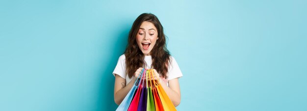 Felice giovane donna guardando le sue borse della spesa con eccitazione che acquista con sconti nei negozi standi