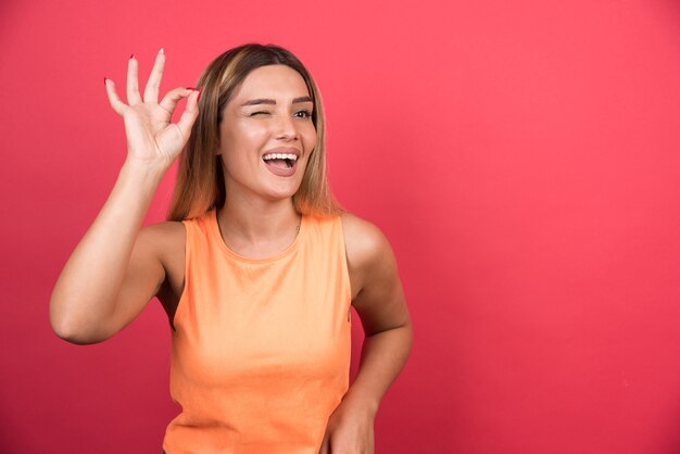 Happy young woman making ok sign on red wall. 