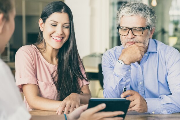 Happy young woman and mature man meeting with professional, watching and discussing content on tablet