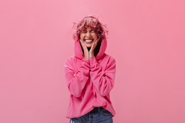 La giovane donna felice in felpa con cappuccio rosa sorride ampiamente su isolato