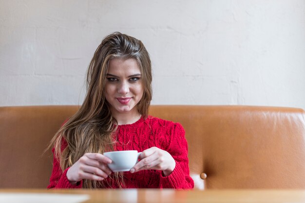 彼女の手の中にコーヒーを飲んでポーズ幸せ若い女性