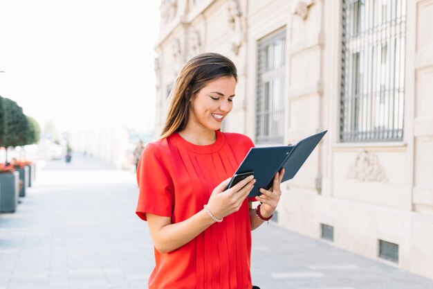 Happy young woman reading diary in city