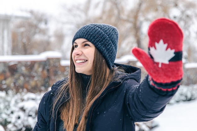雪の降る天気でカナダの旗と赤いミトンで幸せな若い女性