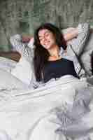 Free photo happy young woman relaxing on soft pillow in the morning