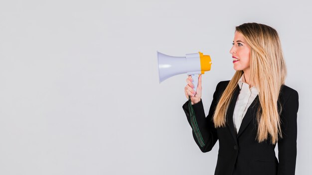 Happy young woman shouting on megaphone against grey background