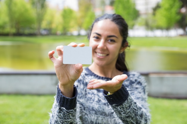 Happy young woman showing blank business card in city park