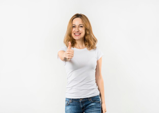 Happy young woman showing thumb up sign looking to camera against white background