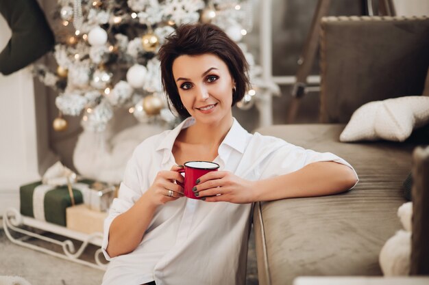 Happy young woman sitting on floor while enjoy hot drink
