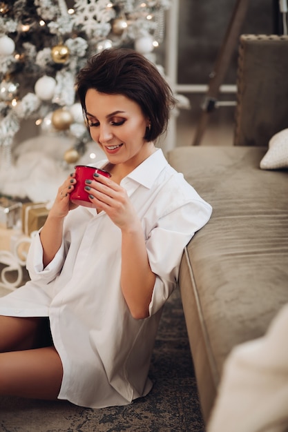 Happy young woman sitting on floor while enjoy hot drink