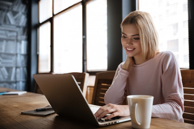 Happy young woman sitting near coffee while work with laptop