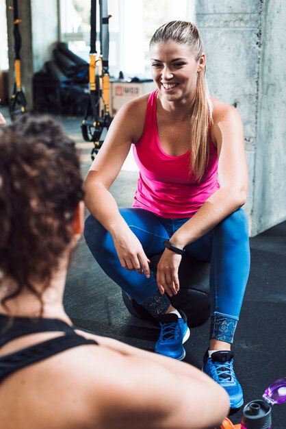 Happy young woman sitting near her friend in gym