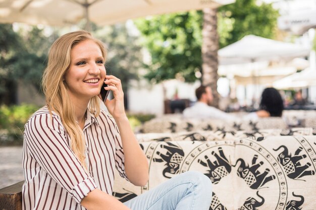 Foto gratuita giovane donna felice che si siede al ristorante all'aperto che parla sul telefono cellulare