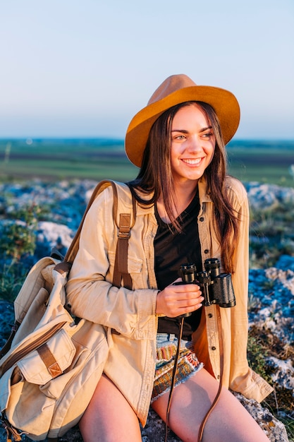 Happy young woman sitting on rock with holding binoculars