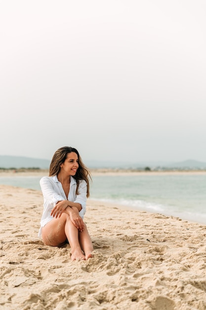 모래 해변에 앉아 행복 한 젊은 여자