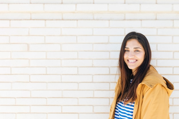 Happy young woman standing against brick wall