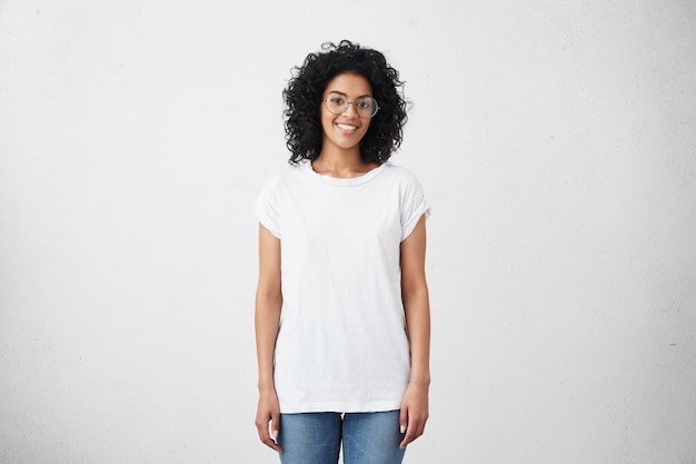 Free photo happy young woman standing at blank white wall