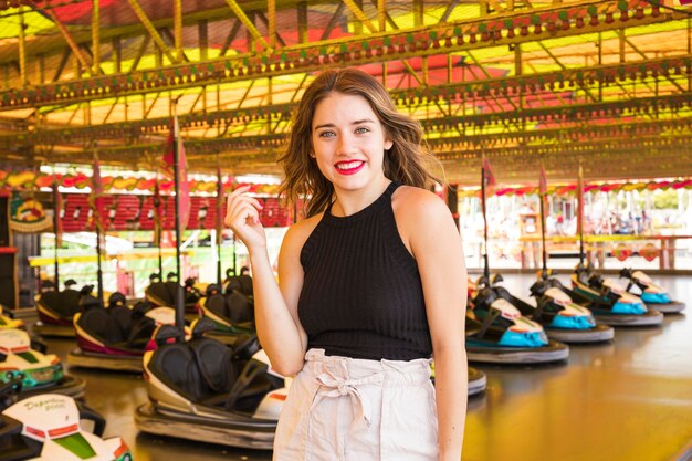 Happy young woman standing in front of bumper car ride at amusement park