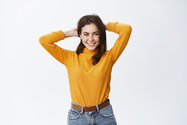 Happy young woman standing relaxed with hands behind head having free time resting and smiling standing on white background