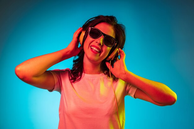 Happy young woman standing and smiling in sunglasses over trendy blue neon studio