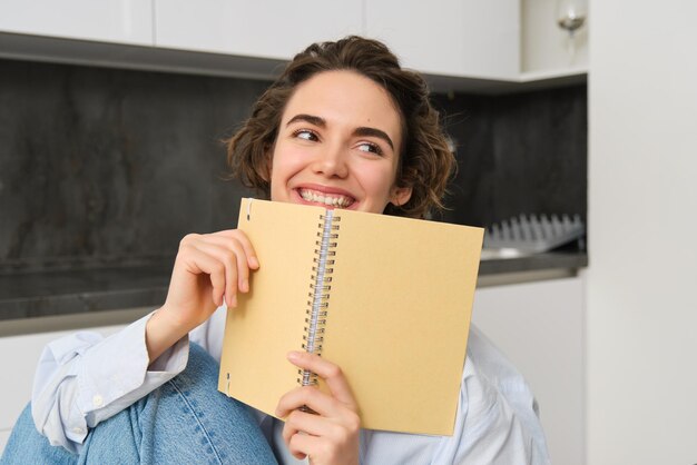 행복 한 젊은 여자 는 집 에서 공부 하고, 저널 을 읽고, 시험 을 준비 하고, 노트북 에 있는 메모 를 보고 있다
