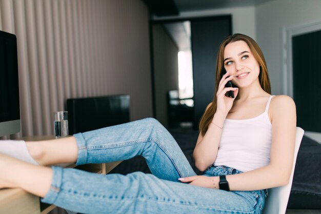 소파에 앉아있는 동안 휴대 전화를 얘기하는 행복 한 젊은 여자