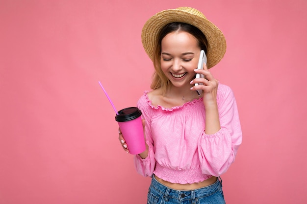 Happy young woman talking on mobile phone while having coffee on pink background
