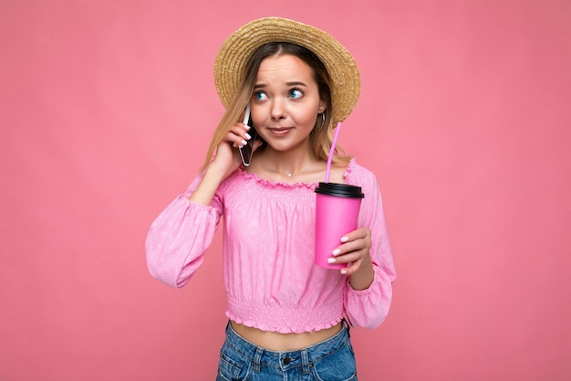 Счастливая молодая женщина разговаривает по мобильному телефону, имея кофе на розовом фоне.