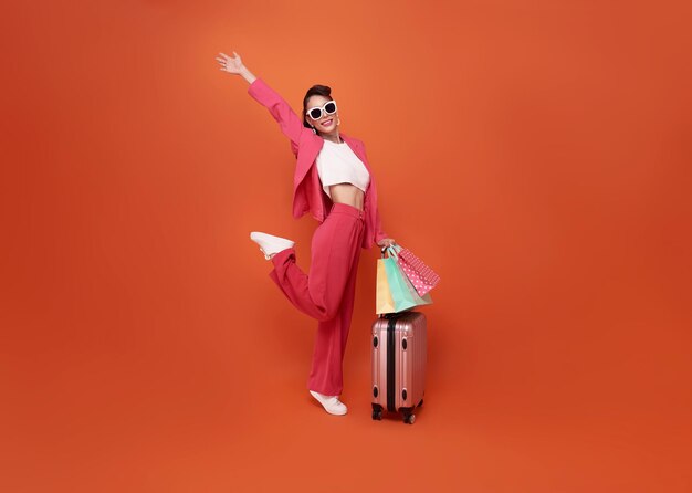 Счастливая молодая женщина-путешественница таскает багаж и сумку с покупками на оранжевом фоне копировального пространства