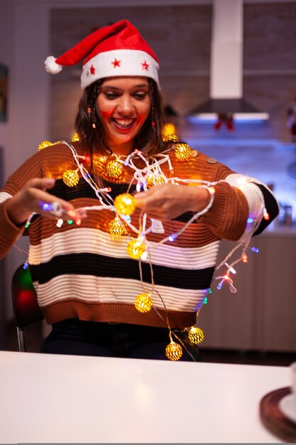 Happy young woman trying to decorate tree with lights