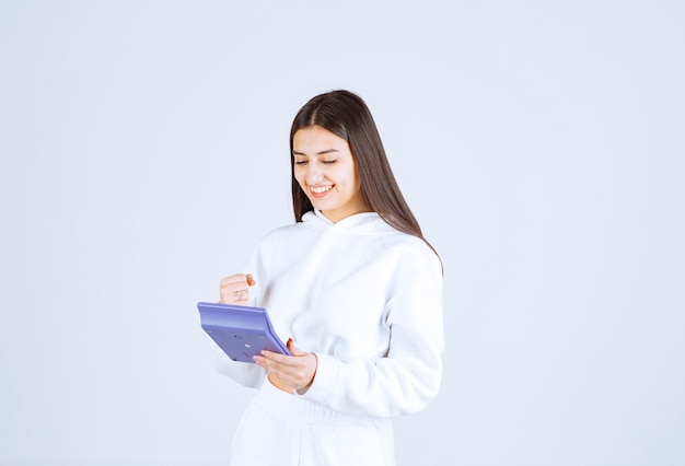 happy young woman using a calculator on white-gray background.