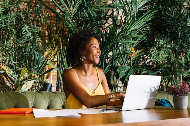 Happy young woman using laptop with documents and digital tablet on wooden table