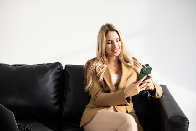 ラップトップコンピューターで自宅のソファに座って携帯電話を使用して幸せな若い女性