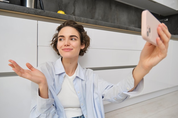 Бесплатное фото Счастливая молодая женщина-блогер записывает видео на своем смартфоне. приложение показывает кухню и ее дом.