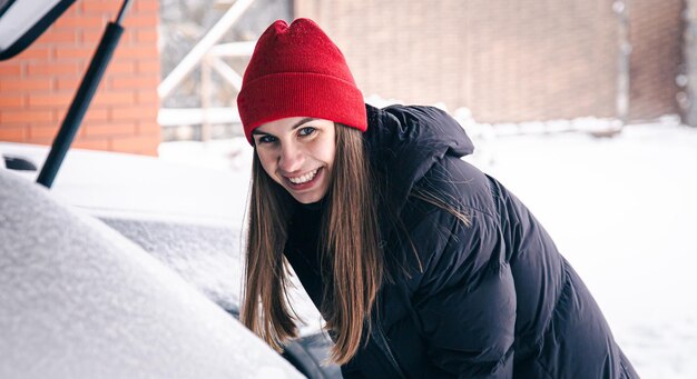Happy young woman in winter gets something from the trunk of a car